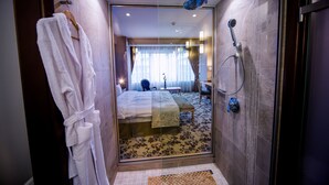 Een moderne badkamer met een douchecabine van glas, een witte badjas aan de muur en een bed met een witte dekbedovertrek en een groene plaid.