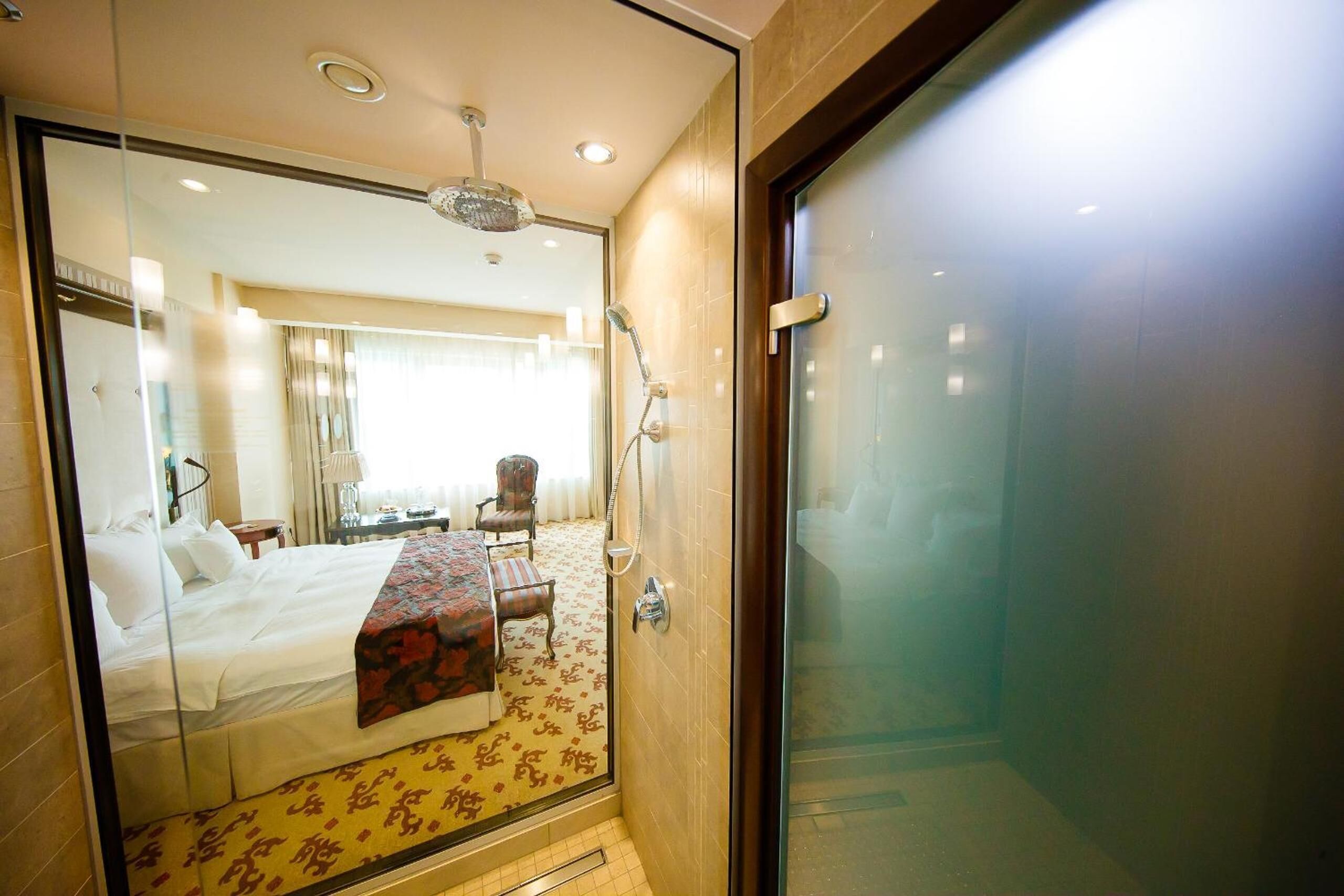 Habitación de hotel con cama, escritorio, silla, zona de ducha y puerta de vidrio.