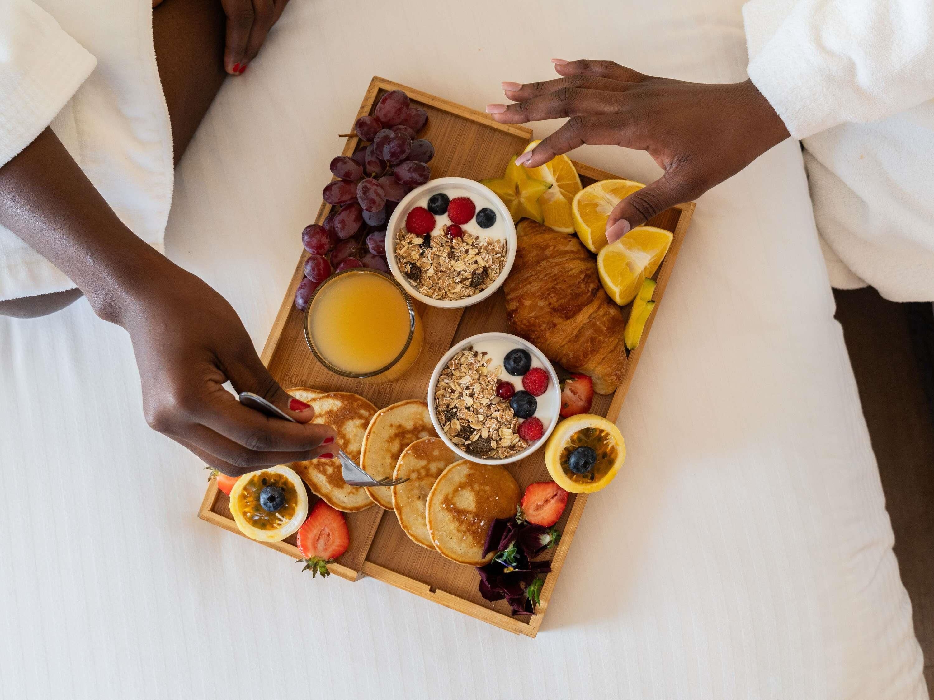 Ein Frühstücksbrett mit Pfannkuchen, Obst, Granola und Saft.