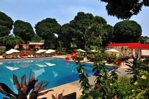 Una piscina rodeada de sillas de descanso y sombrillas, con abundante vegetación al fondo.