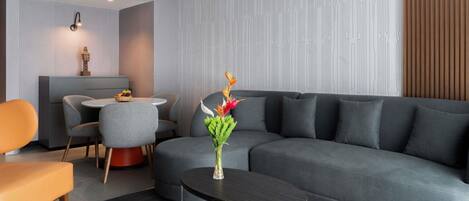 A modern living room with a grey sofa, a round coffee table, a dining area with a small table and chairs, and a decorative plant.
