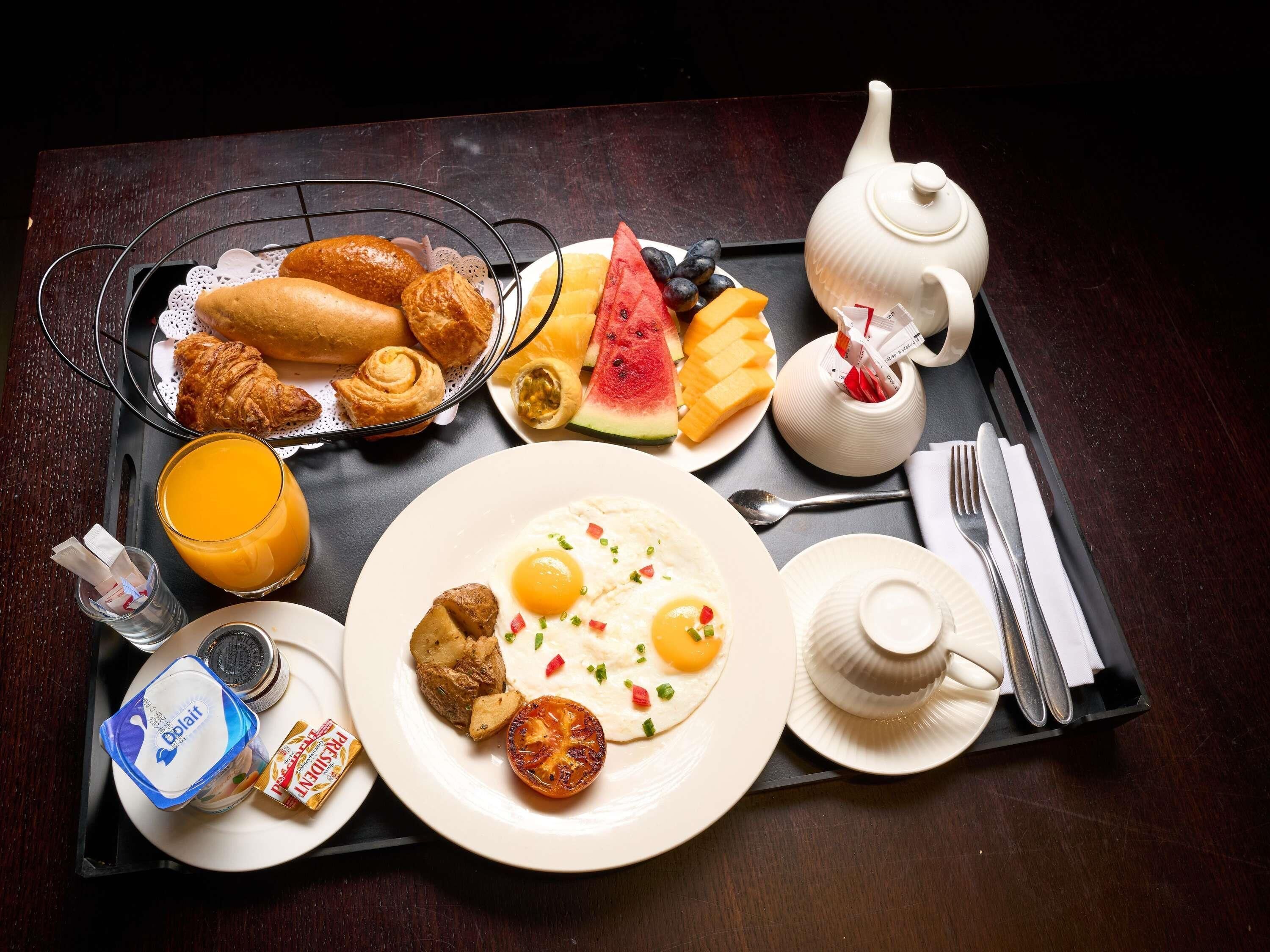 A breakfast tray with croissants, a ham and egg plate, a glass of orange juice, a teapot, and a small container of yogurt.