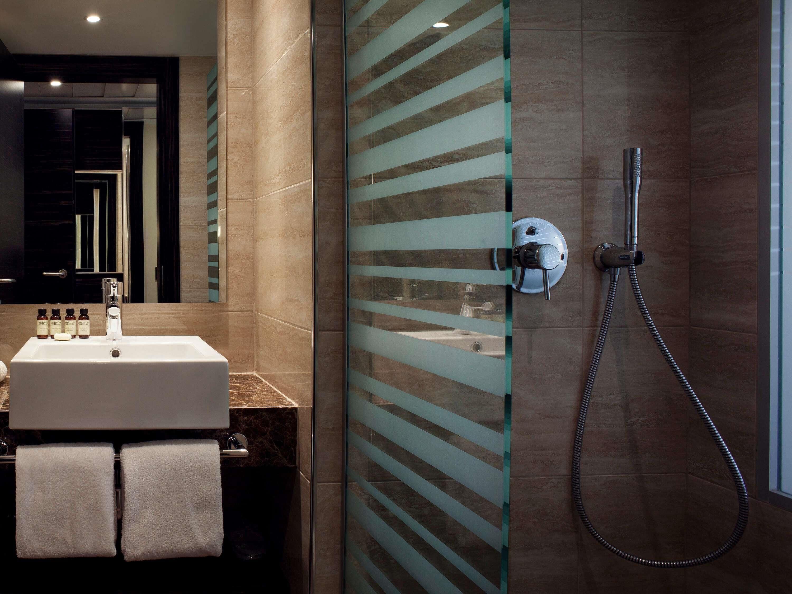 A modern bathroom with a glass shower enclosure, a sink with toiletries, and a large mirror.
