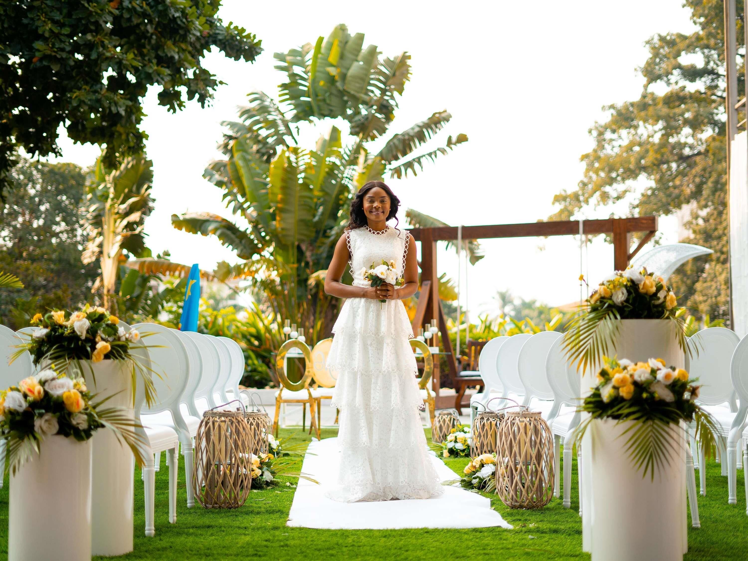 Una ceremonia de boda con una novia en vestido blanco, pasillo bordeado de sillas blancas y centros de mesa florales.
