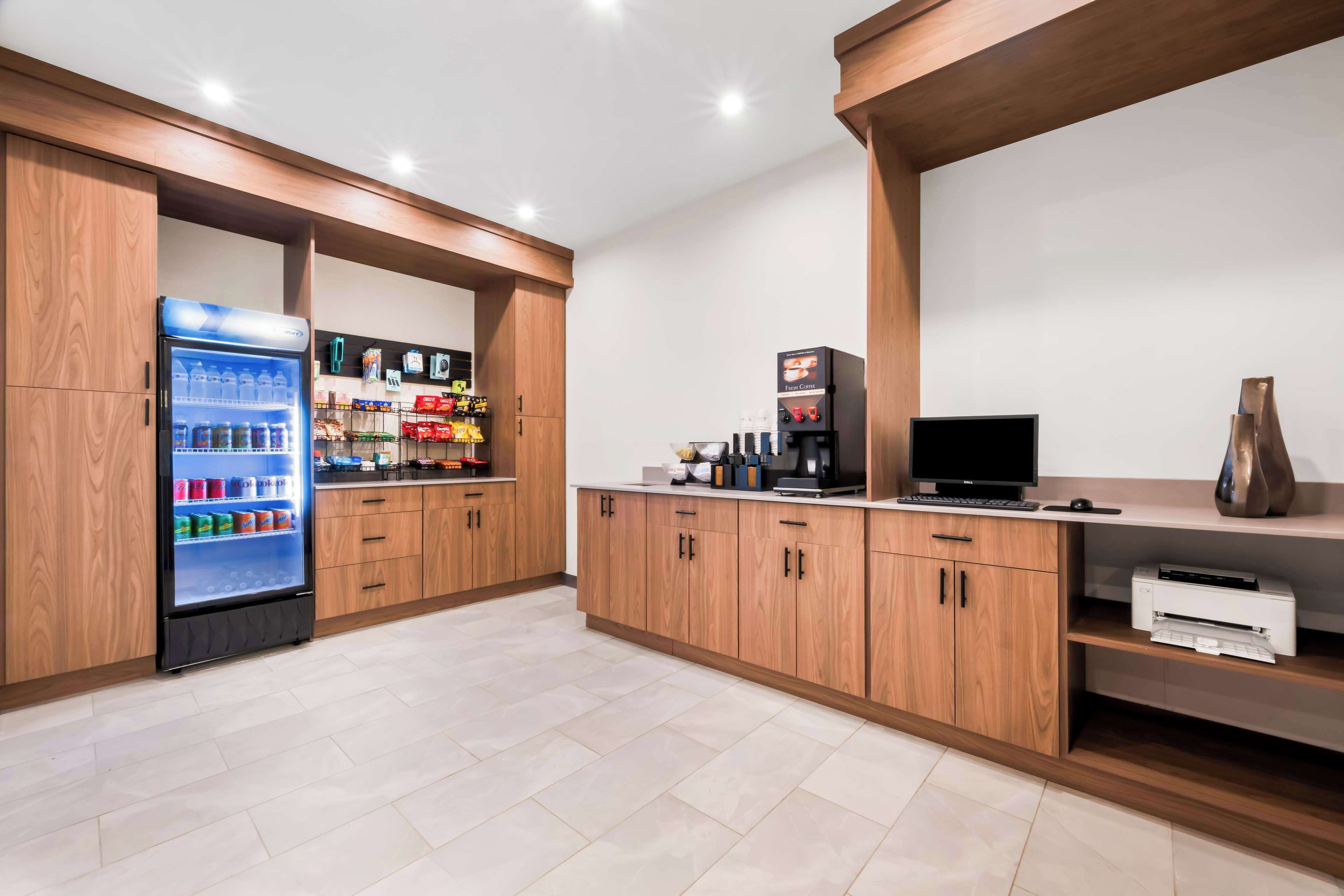 A modern kitchen with wooden cabinets, a refrigerator, a coffee machine, and a flat-screen TV.