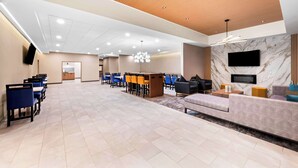 A spacious hotel lobby with a long row of blue chairs, a sofa, a TV mounted on the wall, and a wooden ceiling. - Best Western Niantic - New London/Mystic Area (Niantic)