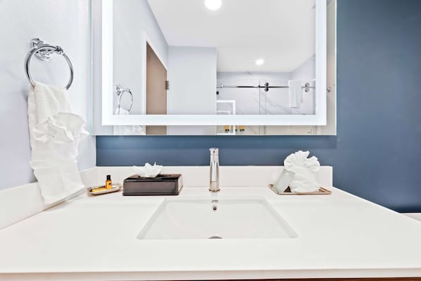 Un baño moderno con un lavabo blanco, un espejo grande y un perchero para toallas.