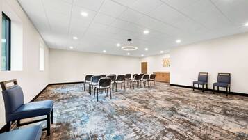 Un salón de conferencias con techo blanco, iluminación empotrada, alfombra estampada y filas de sillas.
