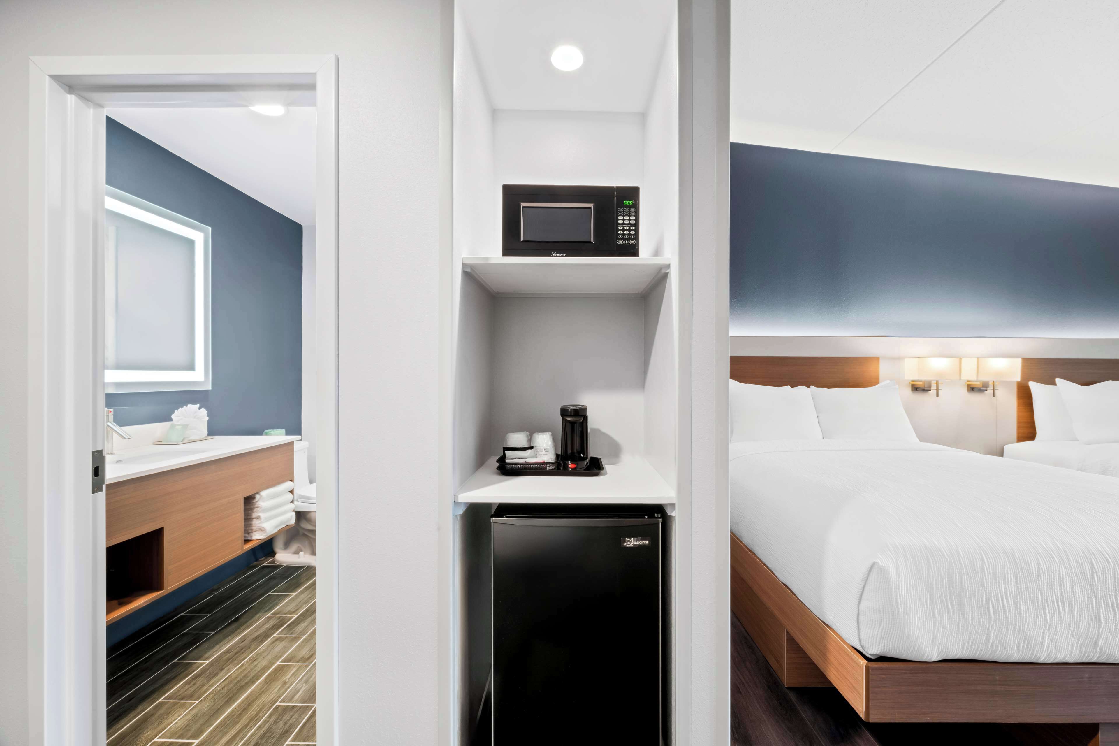 A hotel room with a bed, a microwave, a refrigerator, a sink, and a mirror.