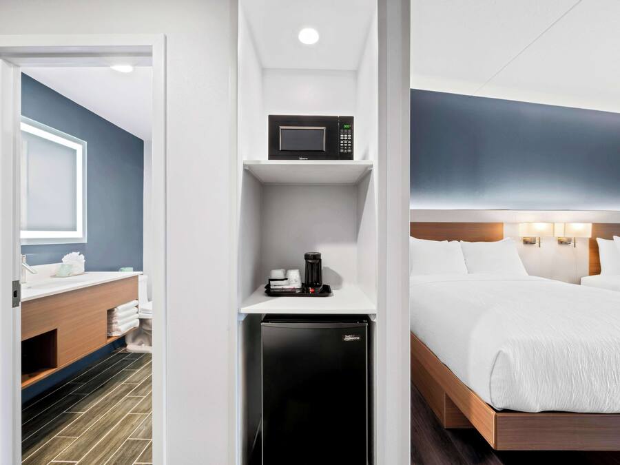 A hotel room with a bed, a microwave, a refrigerator, a sink, and a mirror.
