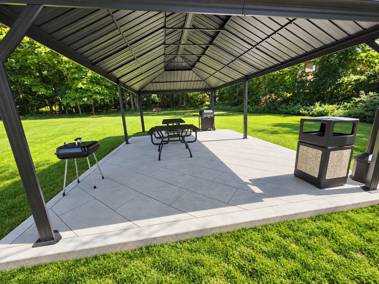 An outdoor patio with a covered seating area, a grill, and a trash can.