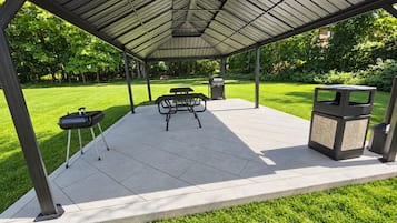 Une terrasse extérieure dotée d’un espace salon couvert, d’un barbecue et d’une poubelle.