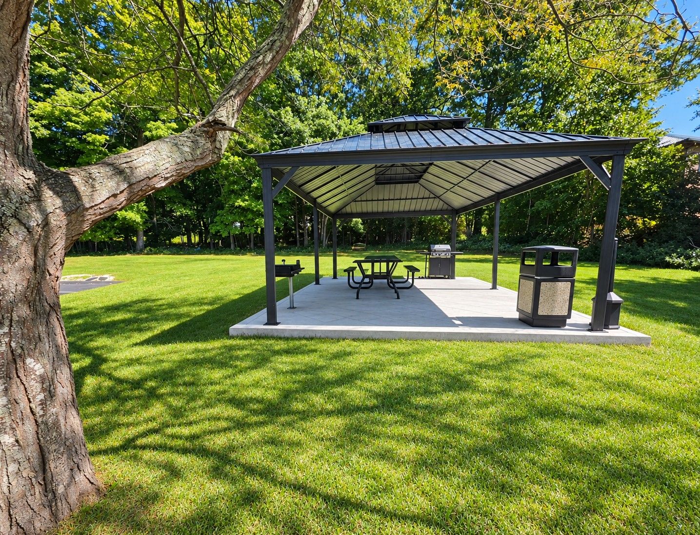 Un área de picnic techada con mesas y bancos, rodeada de césped y árboles.