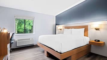 A modern bedroom with a large bed, bedside lamps, a window with blinds, and a built-in heater.