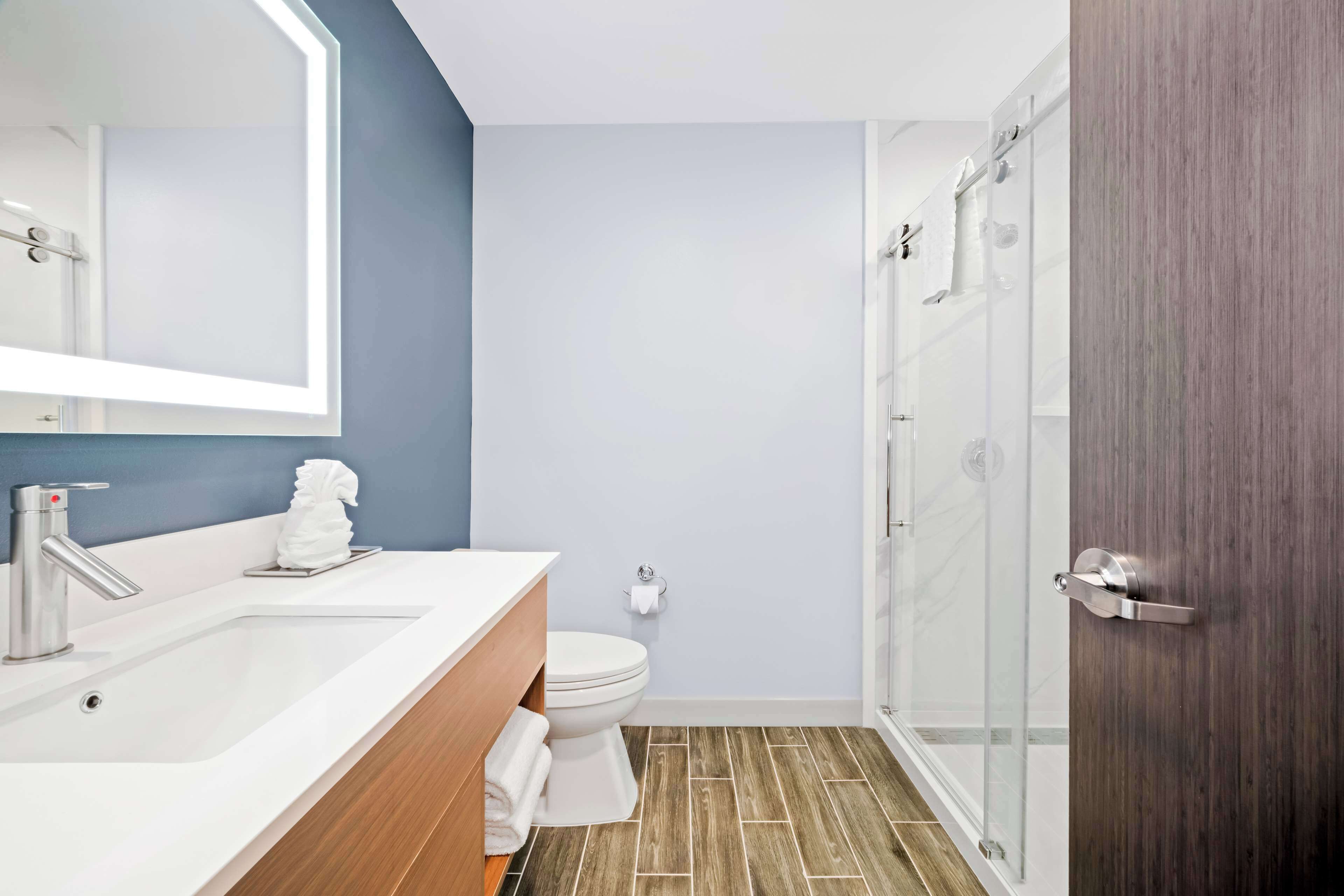 A modern bathroom with a large mirror, a white sink, a toilet, and a glass shower enclosure.