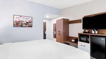 A hotel room with a large bed, a flat-screen TV, a microwave, a refrigerator, a wooden wardrobe, and a painting on the wall.