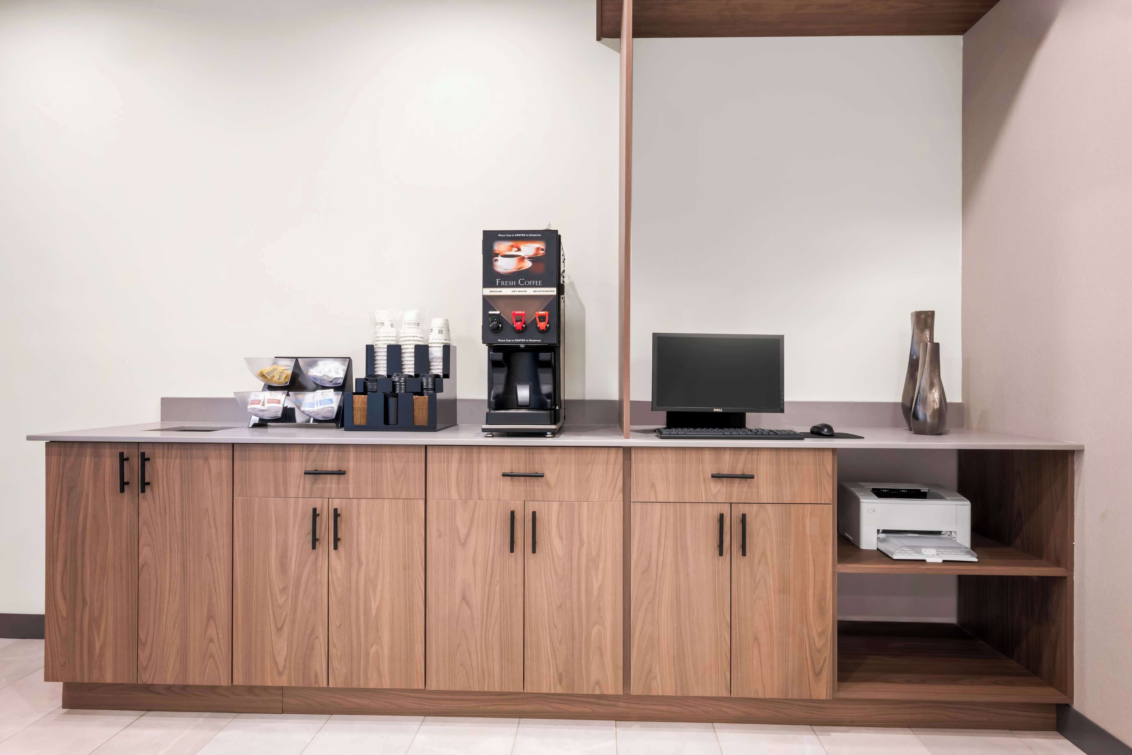 A modern kitchen area with a coffee machine, a computer, and a printer on a wooden countertop.