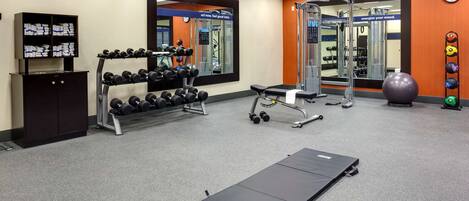 A gym with exercise equipment, a bench, and a mirrored wall.