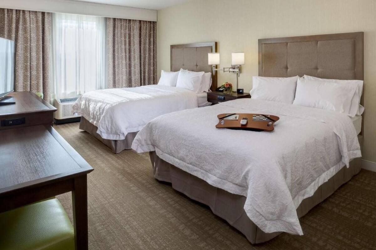 A hotel room with two beds, a desk, and a chair.