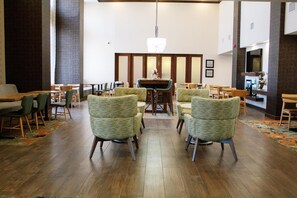 A hotel lobby with a central dining area, multiple seating arrangements, and a large chandelier. - Hampton Inn & Suites Blythe (Blythe)