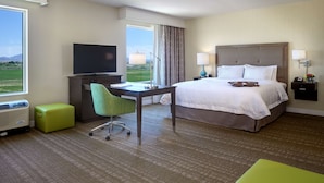 Habitación de hotel con cama, escritorio, silla, televisor, lámpara y vistas al exterior.