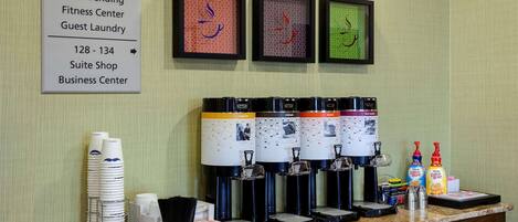 A coffee station with multiple dispensers and a sign listing amenities like meeting rooms, restrooms, and a fitness center.
