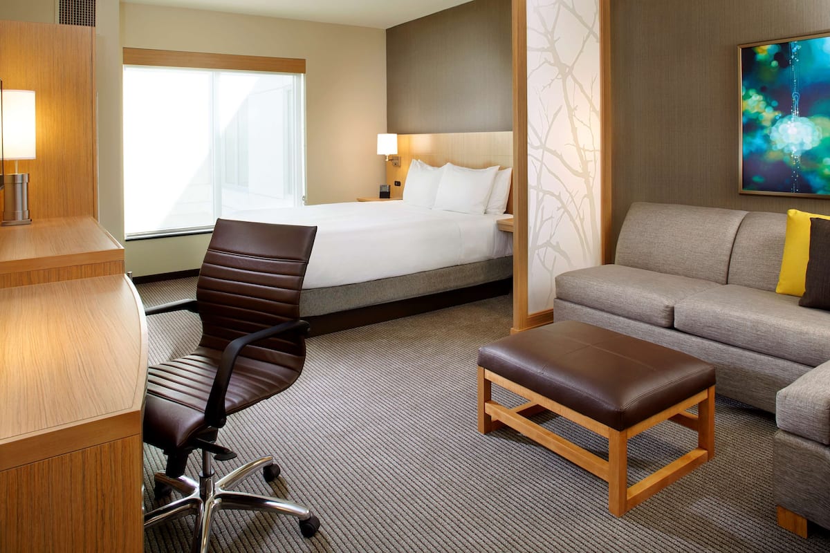 A hotel room with a bed, a desk with a chair, a sofa, and an ottoman.