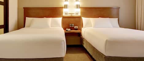 A hotel room with two beds, a wooden headboard, bedside lamps, and a small table with a phone and a lamp.