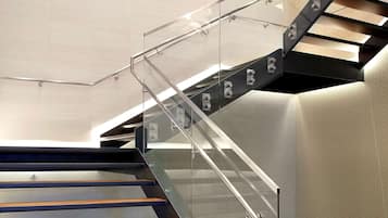 A modern staircase with glass railings, wooden steps, and a unique light fixture.