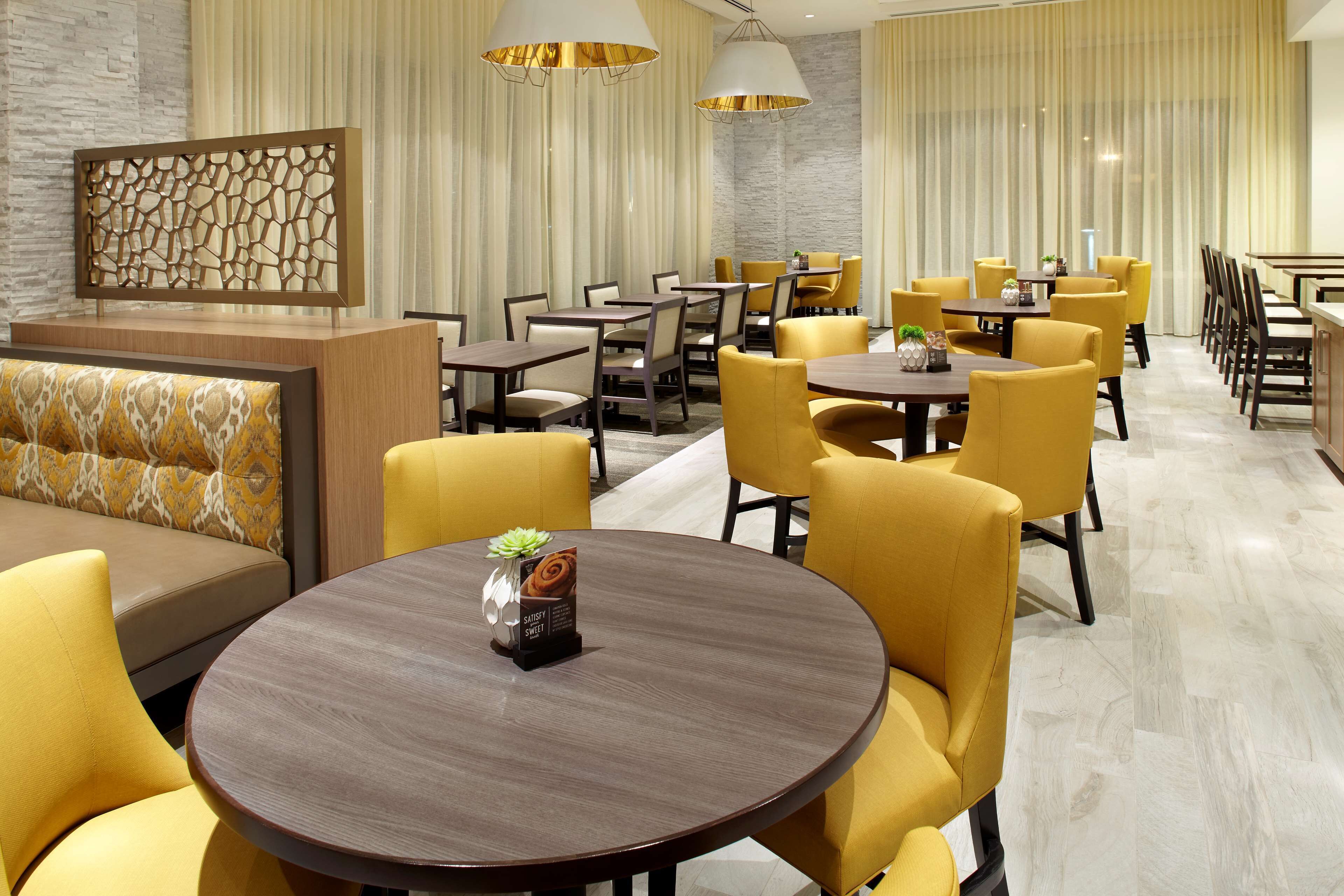A modern dining area with round tables and yellow chairs, a reception desk, and decorative wall panels.