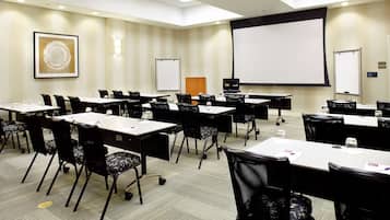 Un salón de conferencias con varias mesas y sillas, una pantalla de proyector y una pizarra.