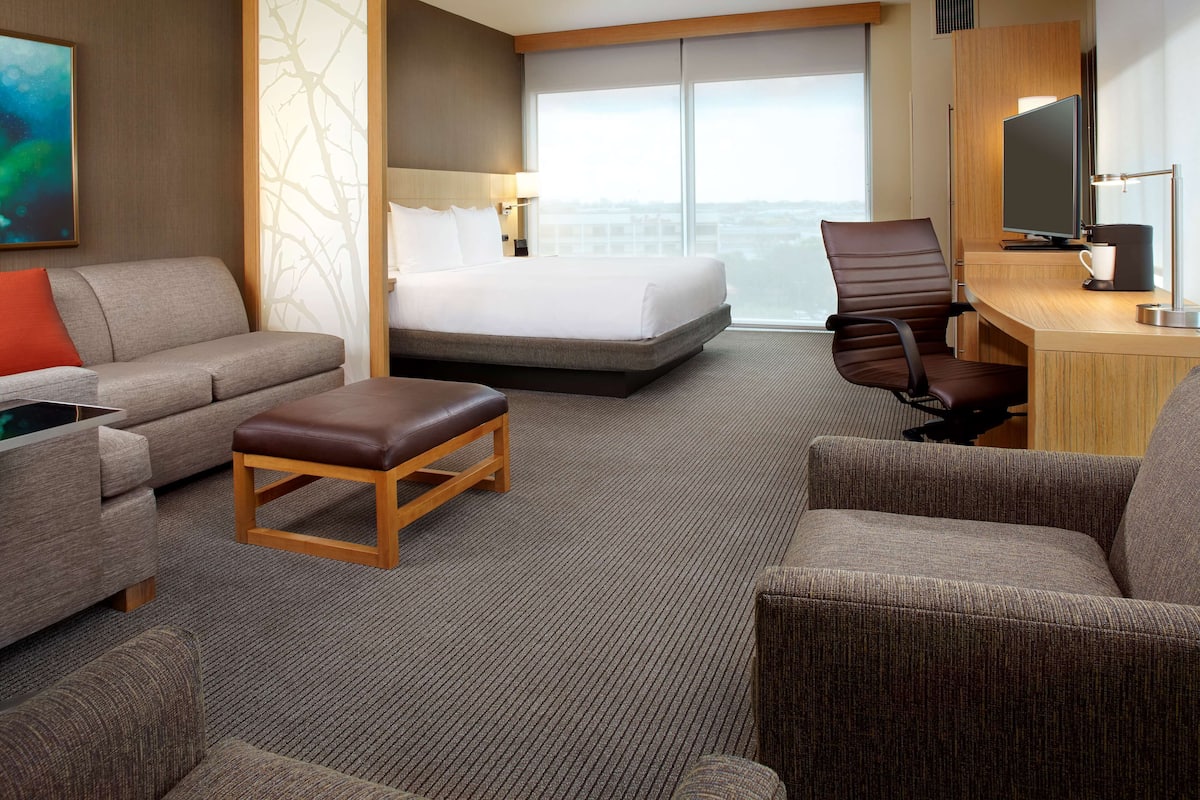 A hotel room with a bed, a desk, a chair, a sofa, and a TV.