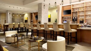 A modern bar area with multiple seating options, a television, and a variety of beverages on display.