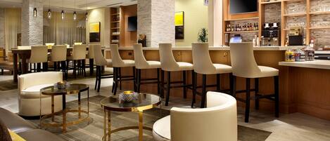 A modern bar area with multiple seating options, a television, and a variety of beverages on display.