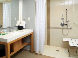Un baño moderno con un lavamanos blanco, tocador de madera, un espejo grande, ducha con cabezal de ducha manual y cerramiento de vidrio.