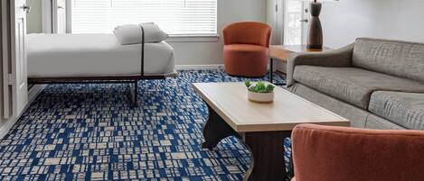 A room with a bed, a sofa, a small table with a plant, and a lamp.