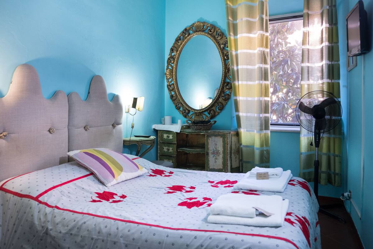 Un dormitorio con cama, cómoda, espejo, ventilador y ventana con cortinas.