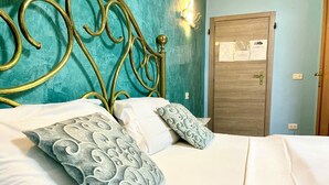 Una cama con ropa de cama blanca y almohadas estampadas, una pared color turquesa y una puerta de madera con interruptor de luz.