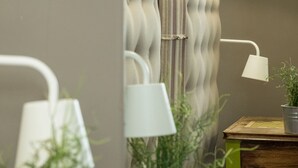 Un baño con cabecera tapizada, dos lámparas de pared, un espejo y una pequeña mesa de madera con una planta.