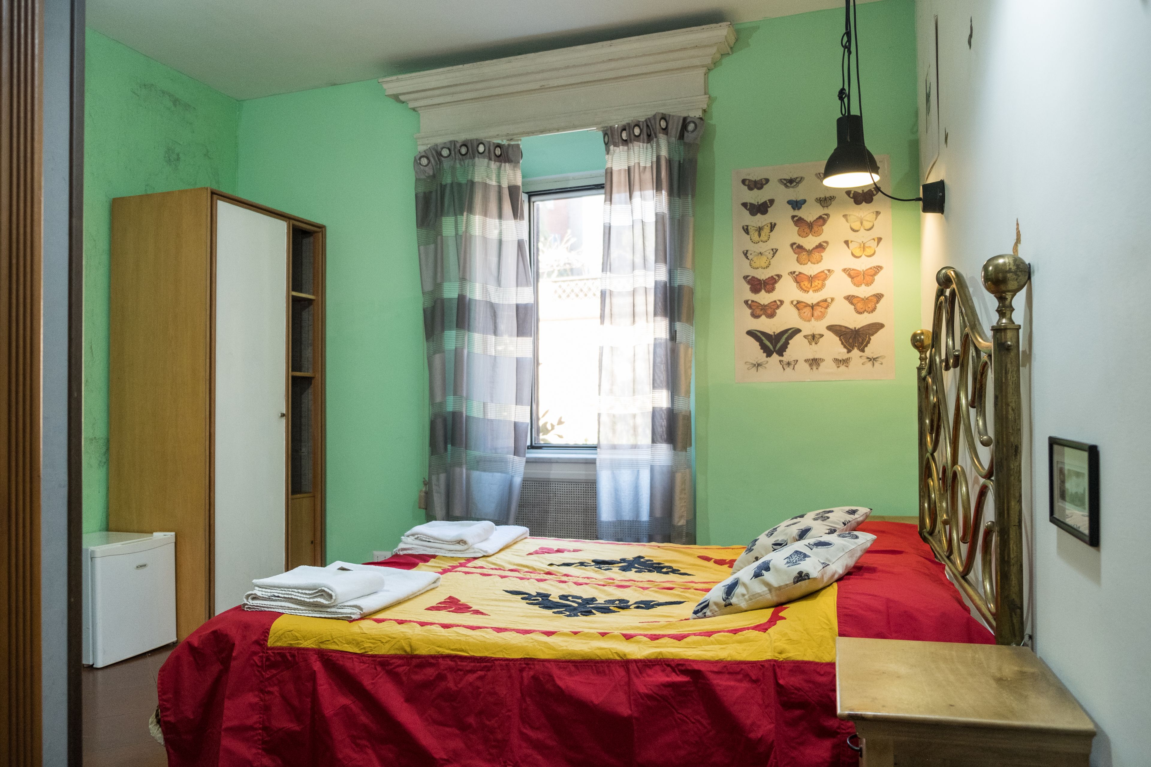 A bedroom with a bed, a wardrobe, a window with curtains, a wall-mounted light, and a butterfly wall art piece.