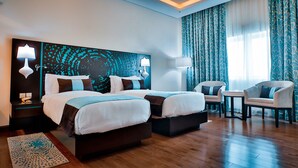 Una habitación de hotel con dos camas, un espacio de descanso con una mesa y un cuadro abstracto grande en la pared.