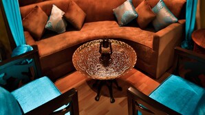Una habitación acogedora con una pared marrón con textura, una mesa redonda con tapa de vidrio y un sofá marrón con cojines estampados.