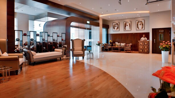 Un vestíbulo amplio con suelo de madera, una zona de estar con sofás y sillones, un mostrador de recepción y un gran ventanal que proporciona luz natural.