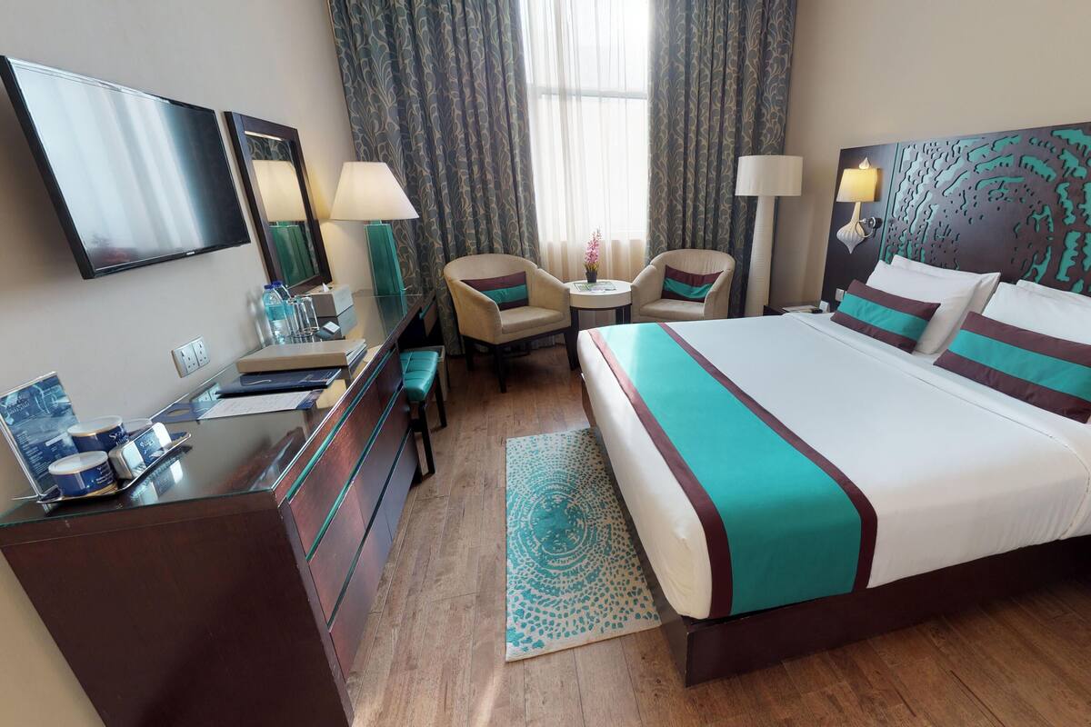 A hotel room with a bed, a desk, a chair, a TV, and a window with curtains.