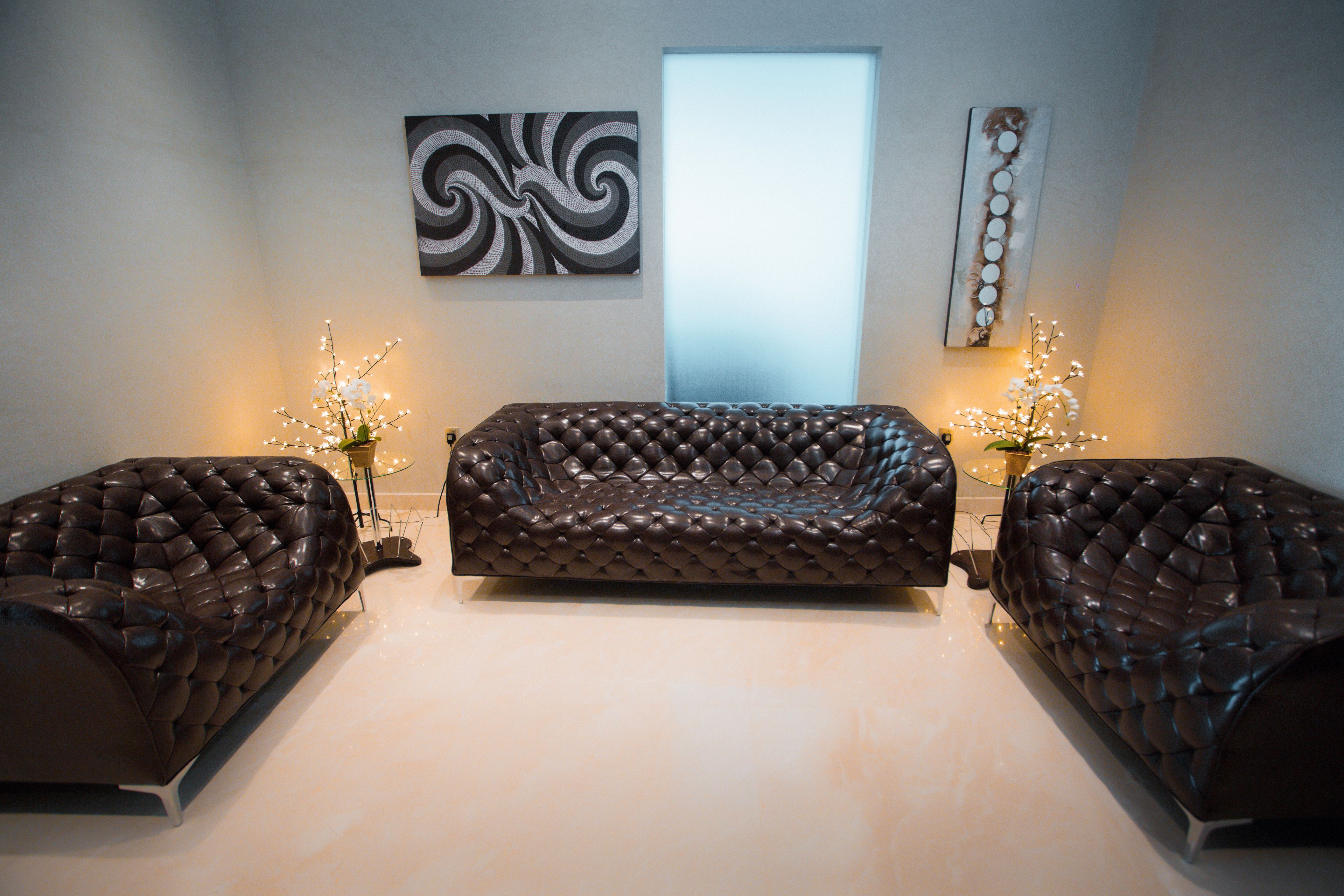 Een modern interieur met een gestuikte leren bank, twee bijzettafels met decoratieve verlichting, en abstracte wanddecoratie.