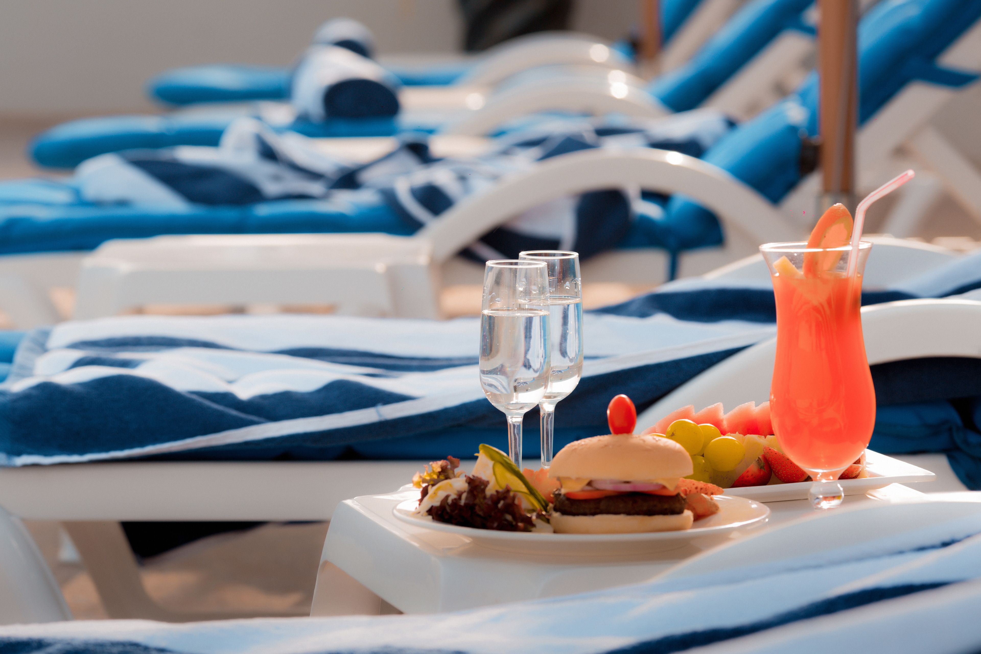 A dining table with a plate of food, two glasses of water, and a pink drink with a straw.