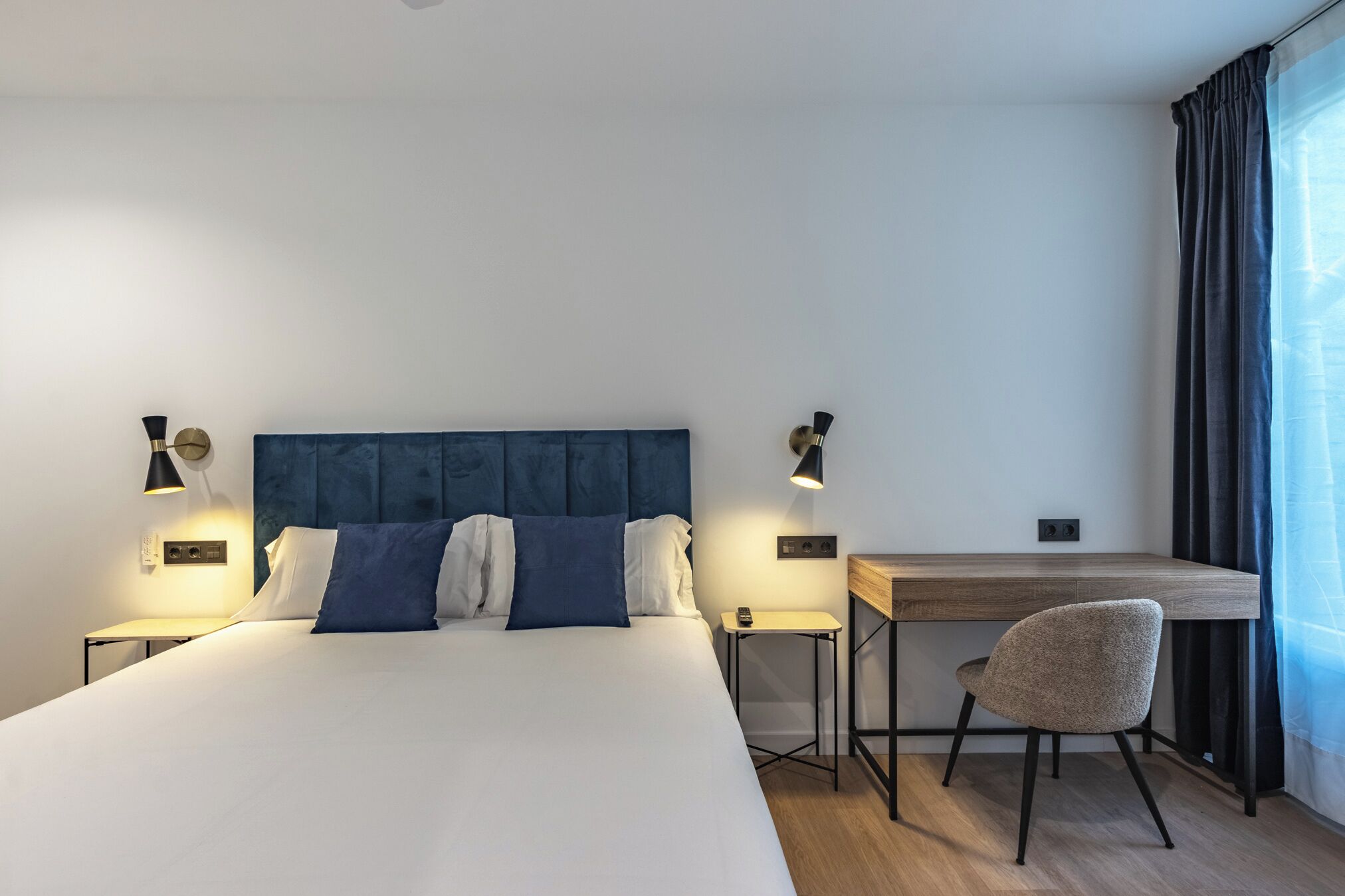 A modern hotel room with a large bed, a desk, and a chair.