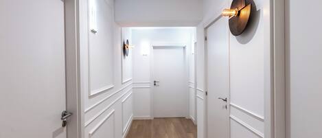 Un pasillo con puertas blancas, suelo de madera y una lámpara fijada a la pared.