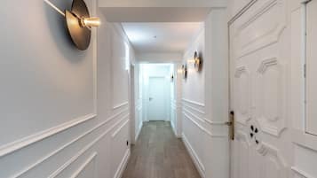 Classic hallway with panelled walls and wooden floor, featuring unique doors and modern lighting.