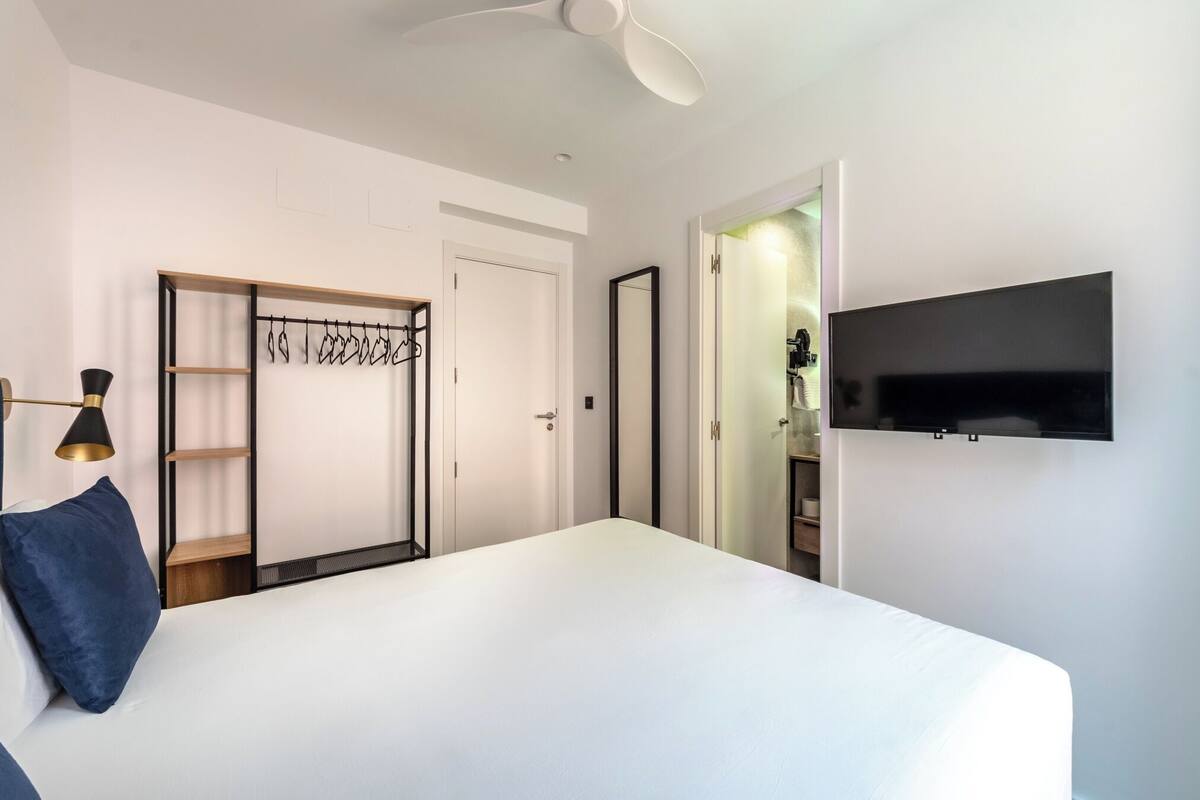 A hotel room with a bed, a wardrobe, a television, and a ceiling fan.